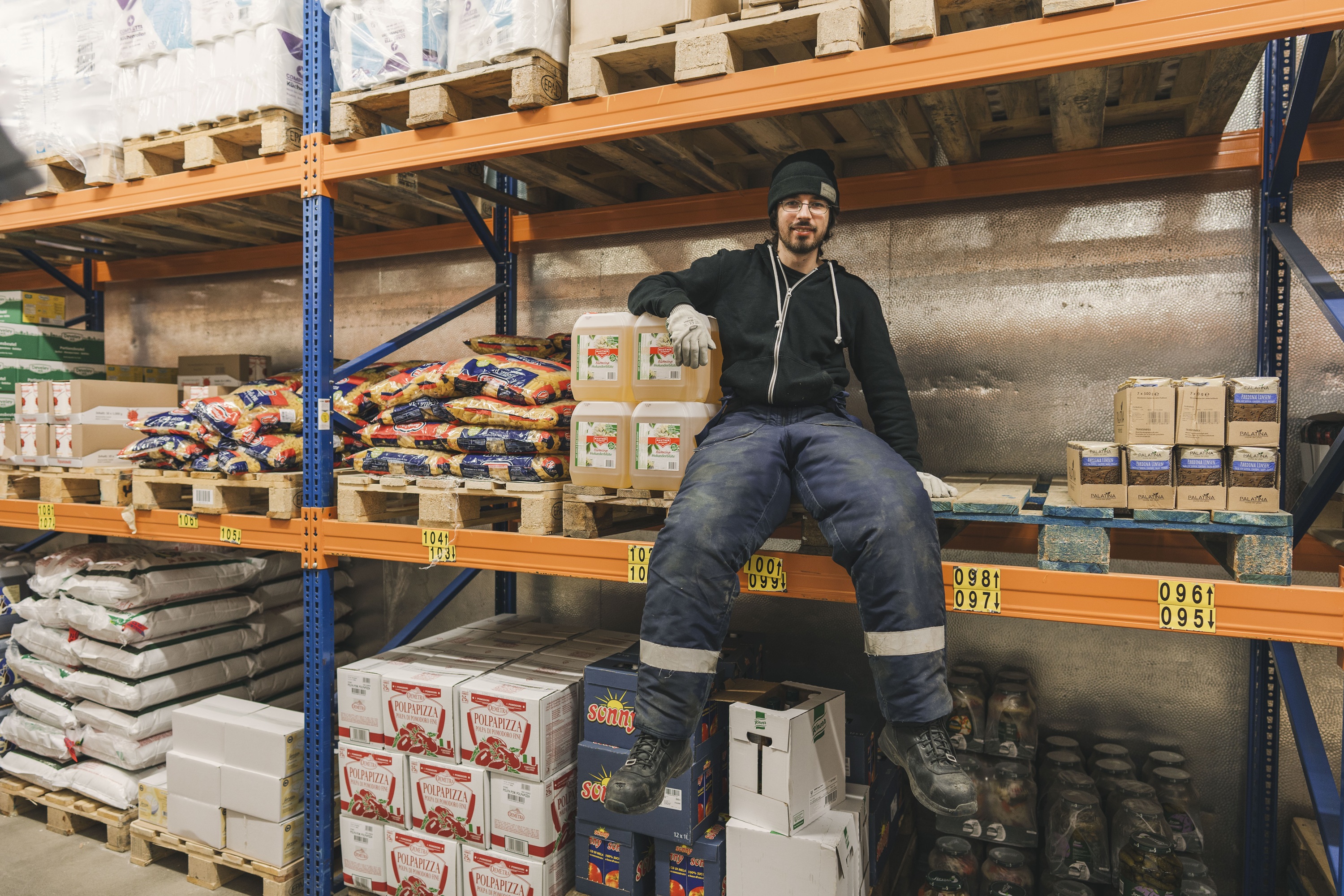 Ein Mann sitzt auf einem Regal in einem Lagerhaus.