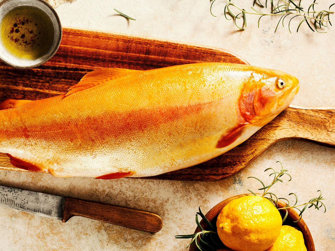 Goldforelle, Huchen, Regenbogenforelle und viele weitere leckere Fische in BQR Qualität erwarten Sie Fisch auf einem Schneidebrett neben Zitronen und einer Schale mit Kräutern